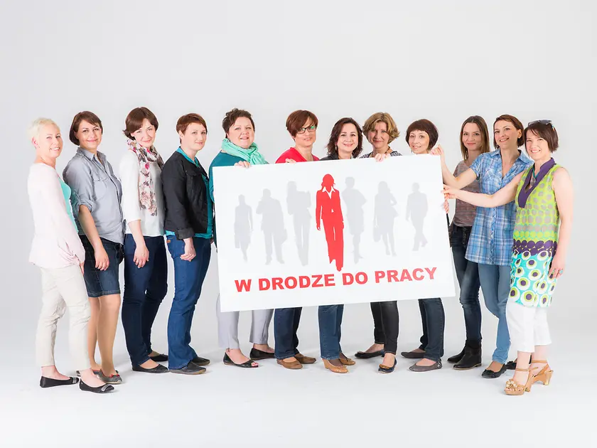 Women standing together with the “W drodze do pracy” sign